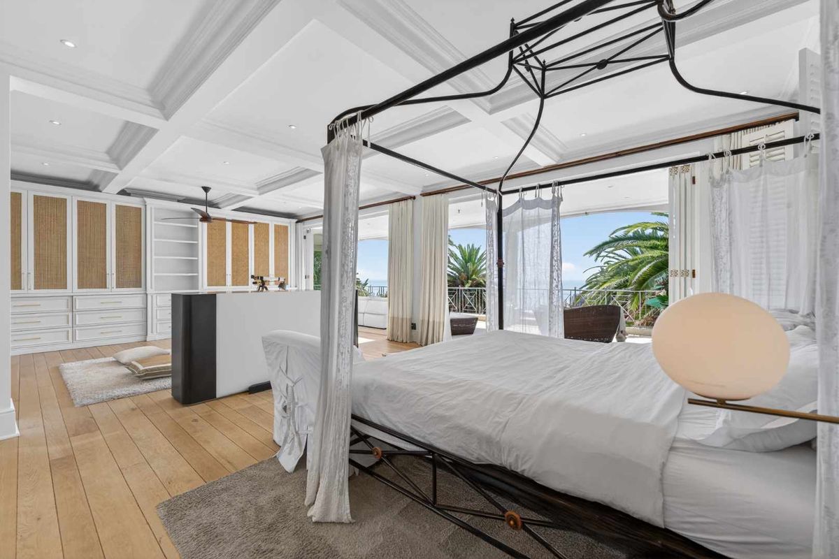 Spacious primary bedroom featuring a coffered ceiling, extensive built-in cabinetry, hardwood floors, and large sliding doors opening to a private balcony with scenic views.