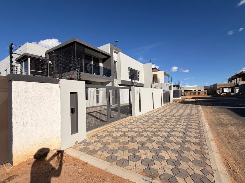 Modern double-story residential property featuring a secure boundary wall, electric fencing, and a paved driveway entrance.