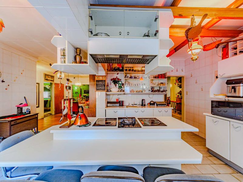 A functional kitchen featuring a central island with a built-in cooktop, overhead extractor fan, tiled surfaces, and exposed timber ceiling beams.
