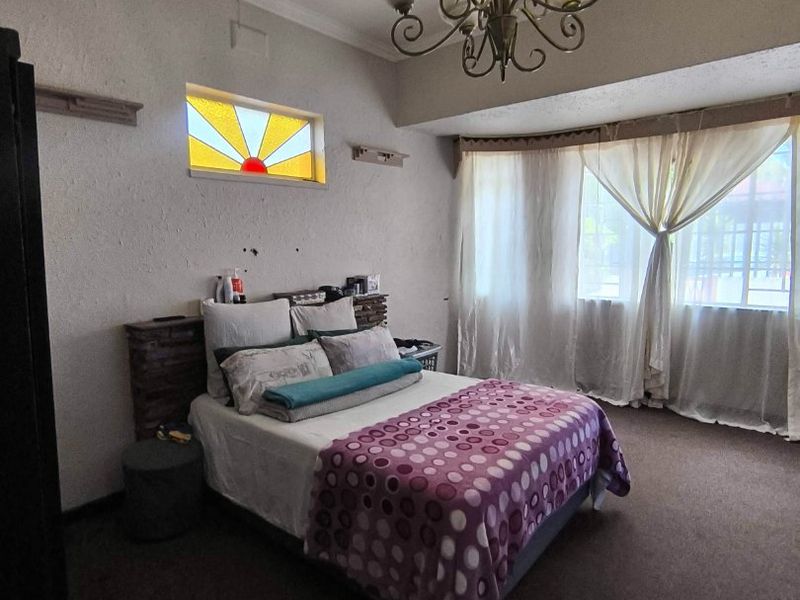 Spacious bedroom featuring a unique stained glass accent window, bay window with natural light, and decorative ceiling cornice.