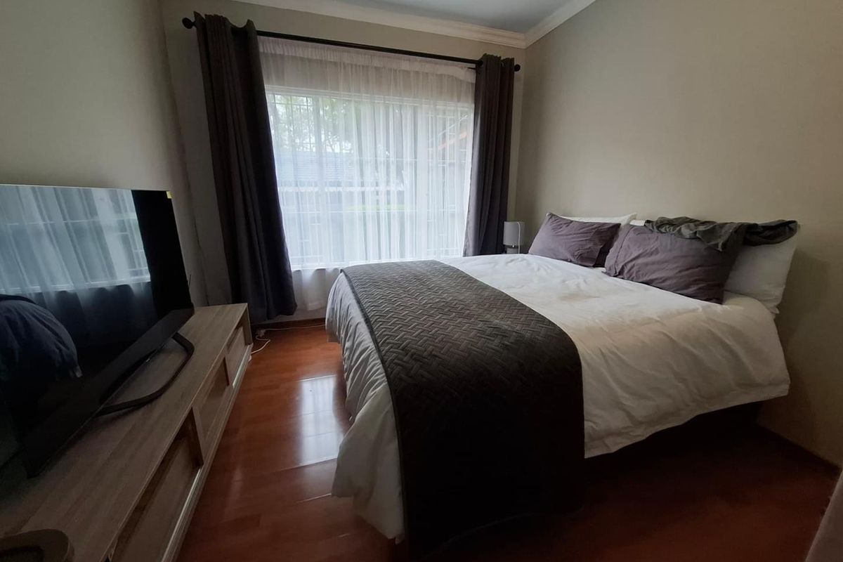 A well-lit bedroom featuring laminate flooring, neutral wall tones, and classic cornicing, providing a comfortable and functional sleeping space.
