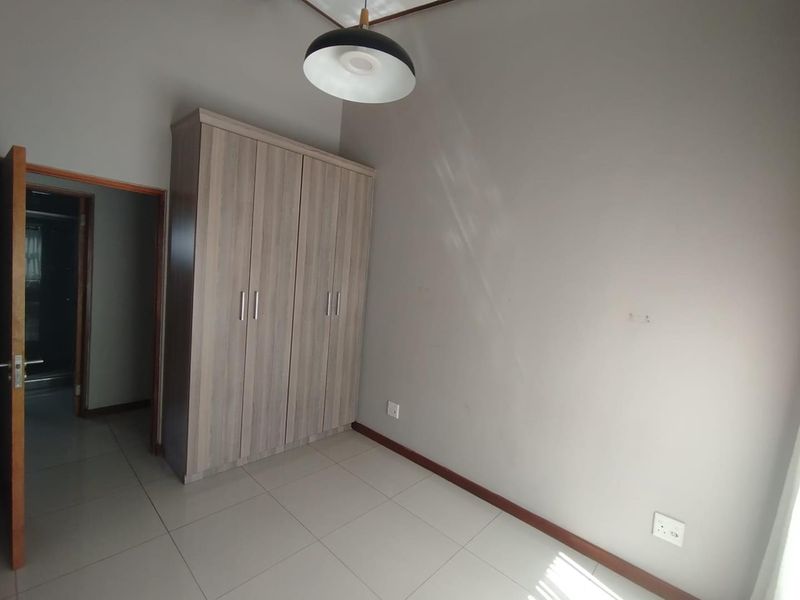 A clean, empty bedroom featuring neutral tiled flooring, a modern built-in wardrobe, and a simple pendant light fixture.