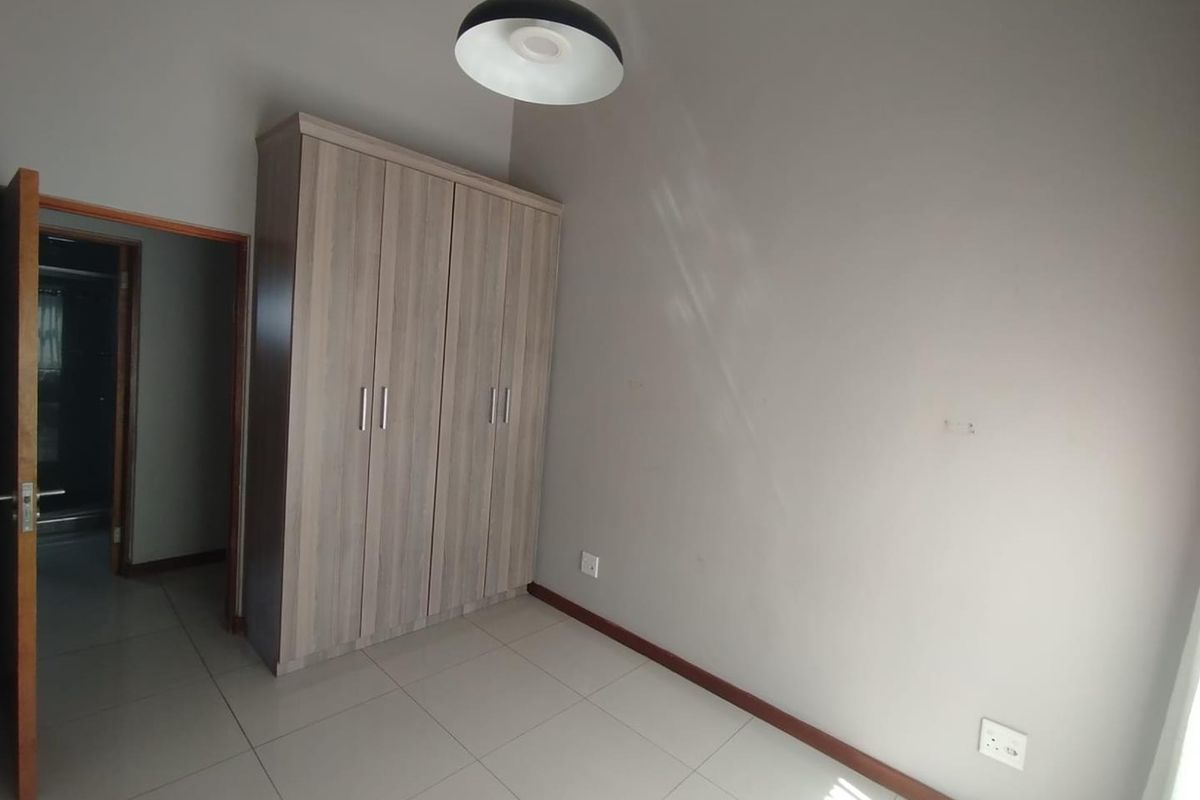 A clean, empty bedroom featuring neutral tiled flooring, a modern built-in wardrobe, and a simple pendant light fixture.
