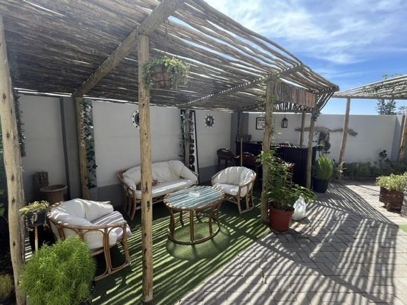 A covered outdoor patio area featuring a rustic timber pergola, paved flooring, and artificial grass, providing a shaded space for relaxation.