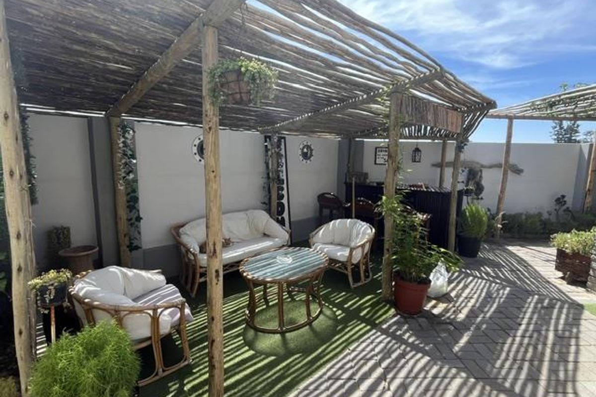 A covered outdoor patio area featuring a rustic timber pergola, paved flooring, and artificial grass, providing a shaded space for relaxation.