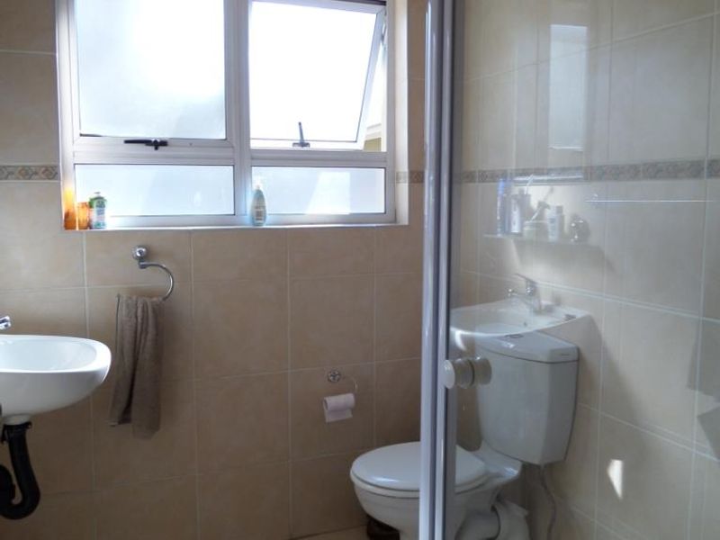 A functional bathroom featuring a shower enclosure, pedestal basin, and toilet with neutral wall and floor tiling.