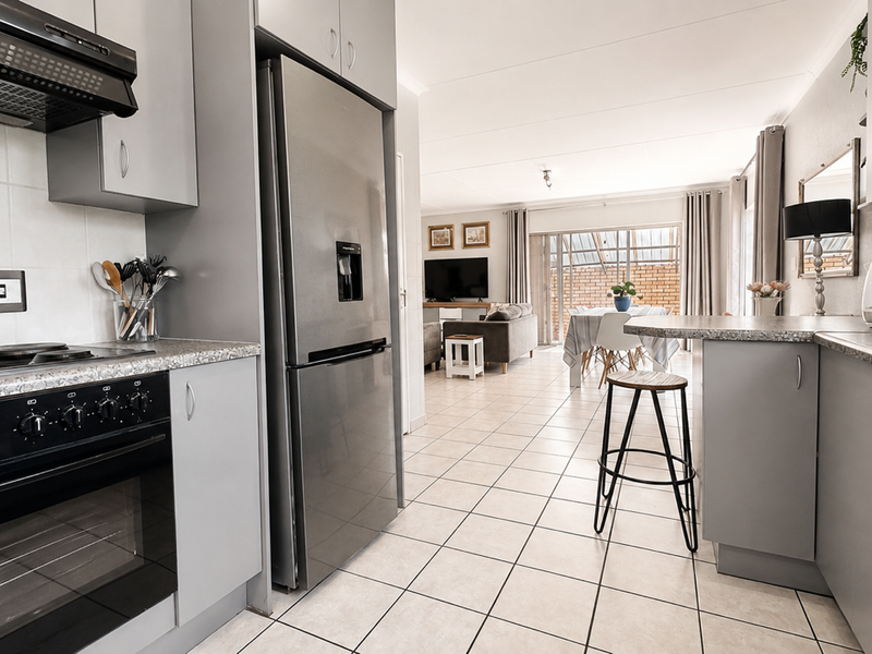 Open-plan kitchen featuring modern grey cabinetry, laminate countertops, and a breakfast bar, flowing seamlessly into the adjacent living and dining area.