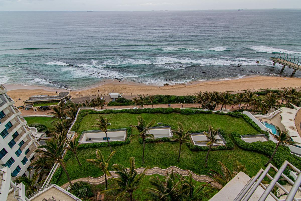 Elevated aerial view overlooking the coastal landscape, featuring a landscaped green roof area, beach access, and expansive ocean vistas.