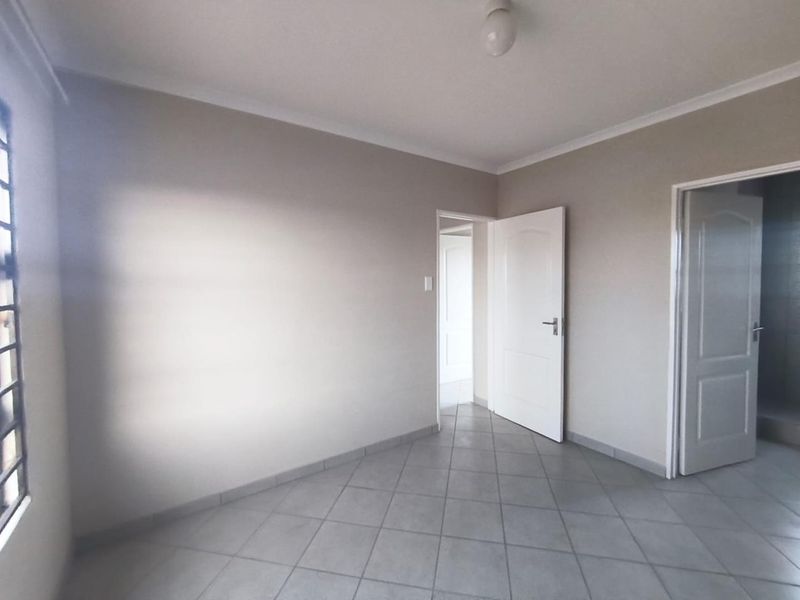 A clean, empty bedroom featuring neutral wall paint, tiled flooring, and coved ceilings, providing a versatile space ready for personalization.
