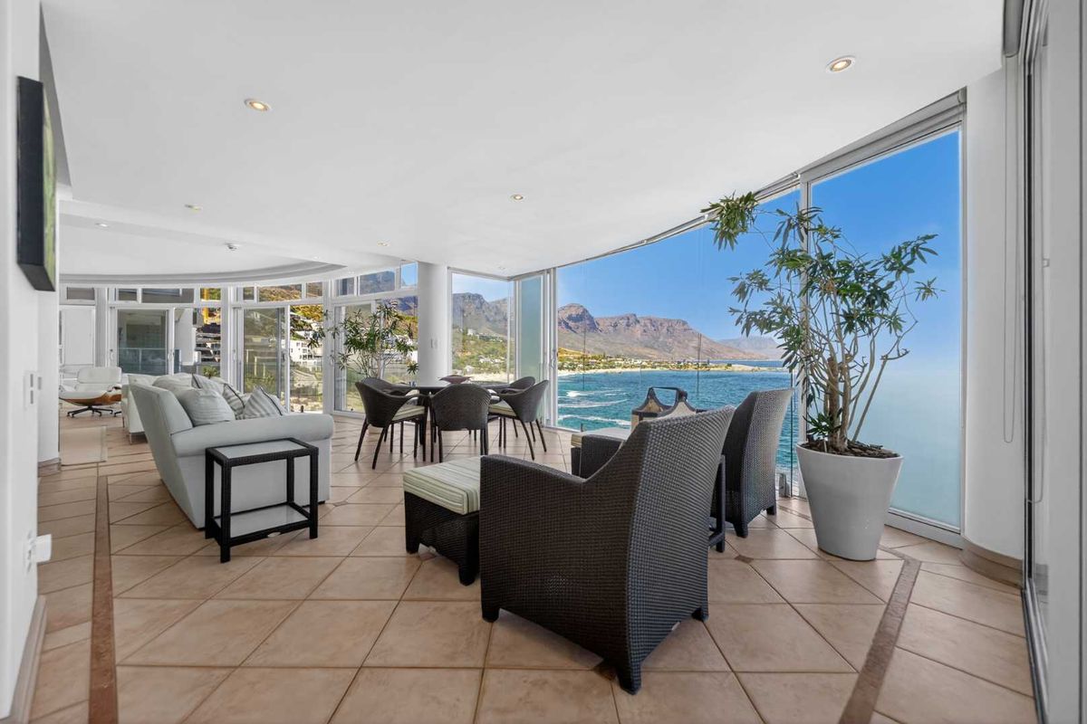 Spacious open-plan living area featuring floor-to-ceiling glass doors that offer panoramic ocean and mountain views, complemented by neutral ceramic tiling and recessed lighting.