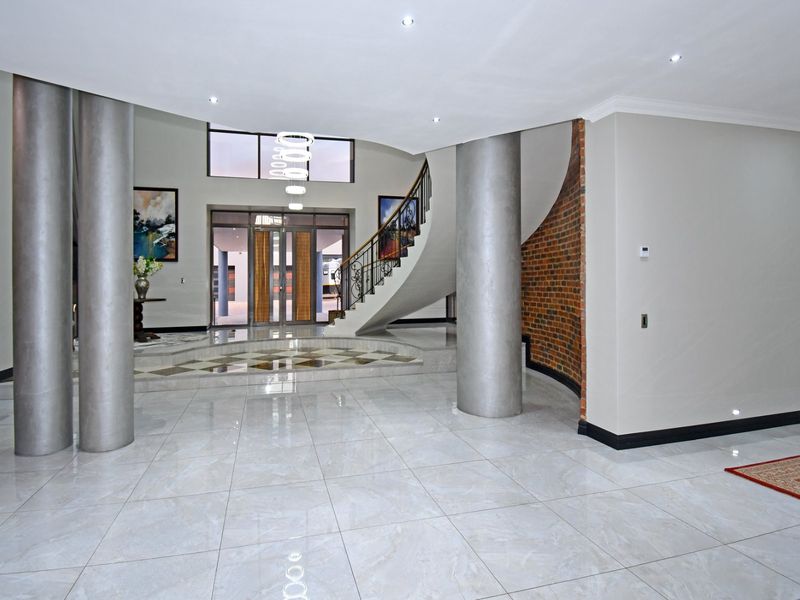 Spacious grand entrance hall featuring a curved staircase with wrought iron balustrade, polished tiled flooring, and an exposed brick feature wall.