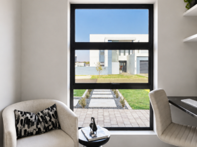 A bright, modern home office featuring tiled flooring, built-in shelving, and a large window with views of the front garden.
