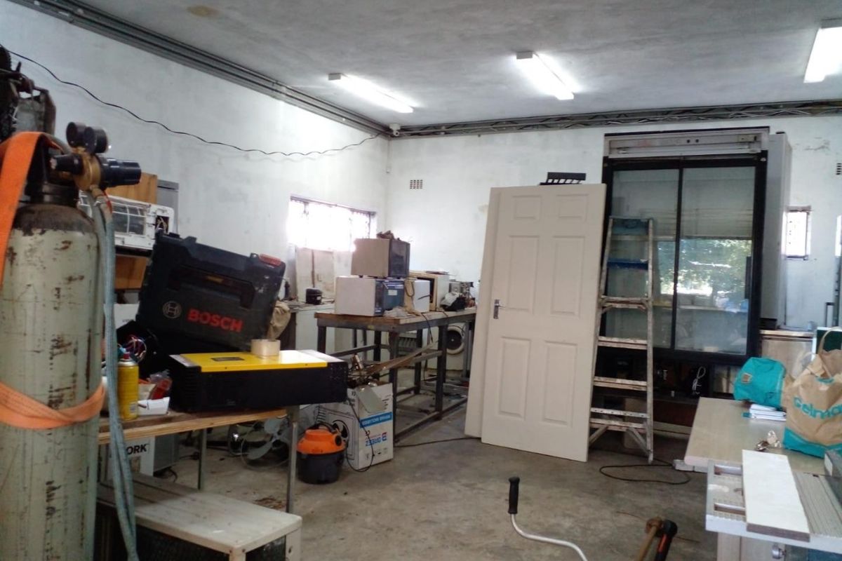 A functional utility or workshop space featuring concrete flooring, fluorescent lighting, and exposed electrical conduit, suitable for storage or industrial use.