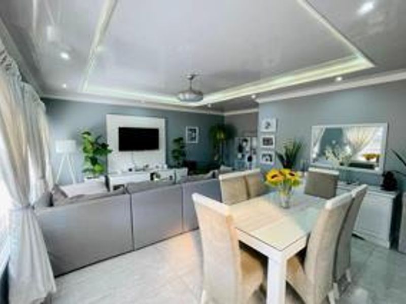 Spacious open-plan living and dining area featuring a modern recessed ceiling, tiled flooring, and a dedicated built-in media wall.