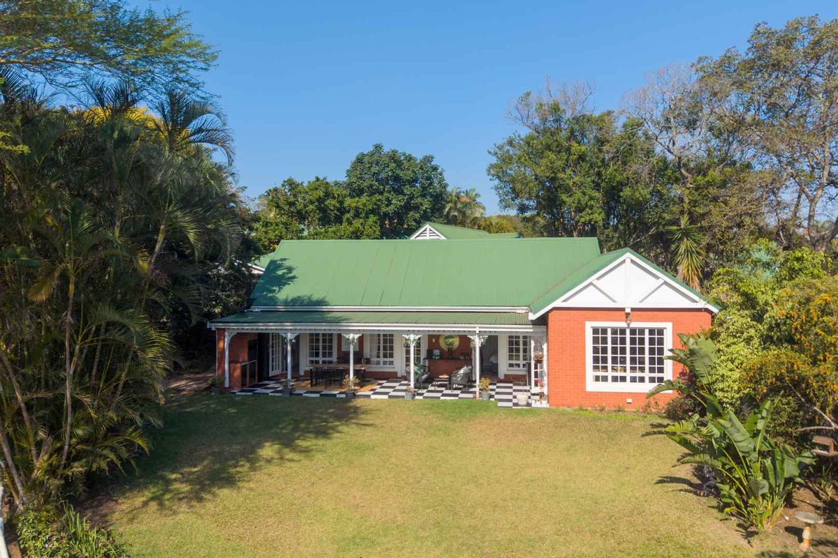 A well-maintained rear elevation featuring a red brick facade, green metal roof, and a spacious covered patio with classic checkered tile flooring.