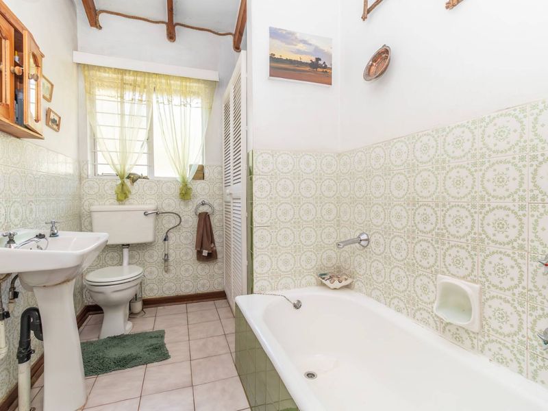 A dated bathroom featuring a pedestal basin, close-coupled toilet, and a built-in bathtub with vintage patterned wall tiles.