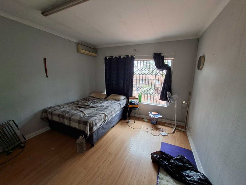 A bedroom featuring laminate flooring, an air conditioning unit, and a window fitted with a security gate.