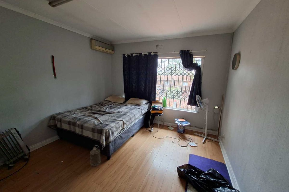 A bedroom featuring laminate flooring, an air conditioning unit, and a window fitted with a security gate.