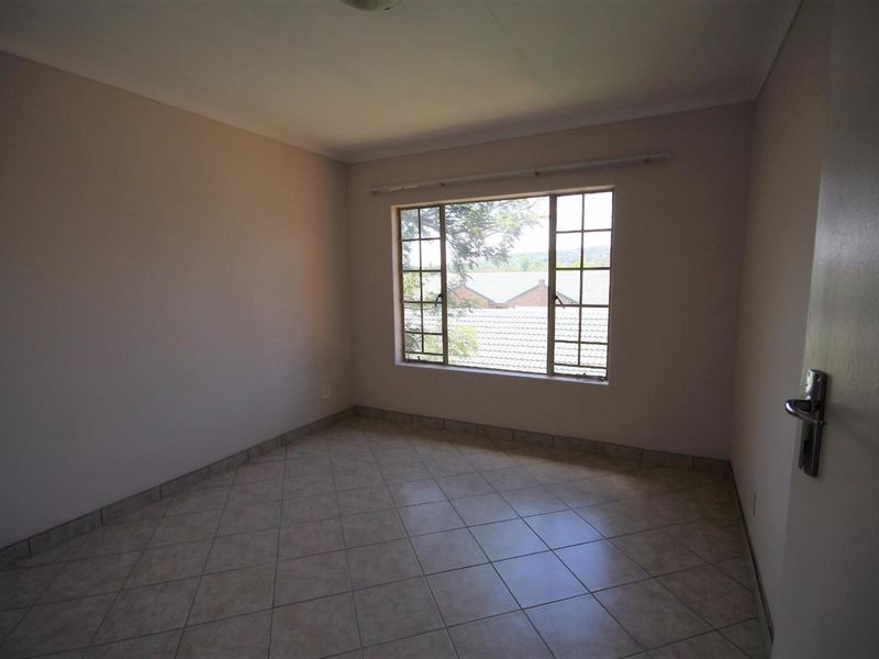 An empty bedroom featuring neutral walls, tiled flooring, and a window with security bars, offering a blank canvas for personalization.