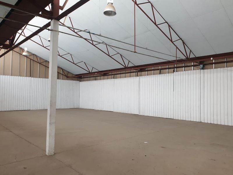 Spacious industrial utility area featuring high ceilings with exposed steel trusses, corrugated metal wall cladding, and durable concrete flooring.