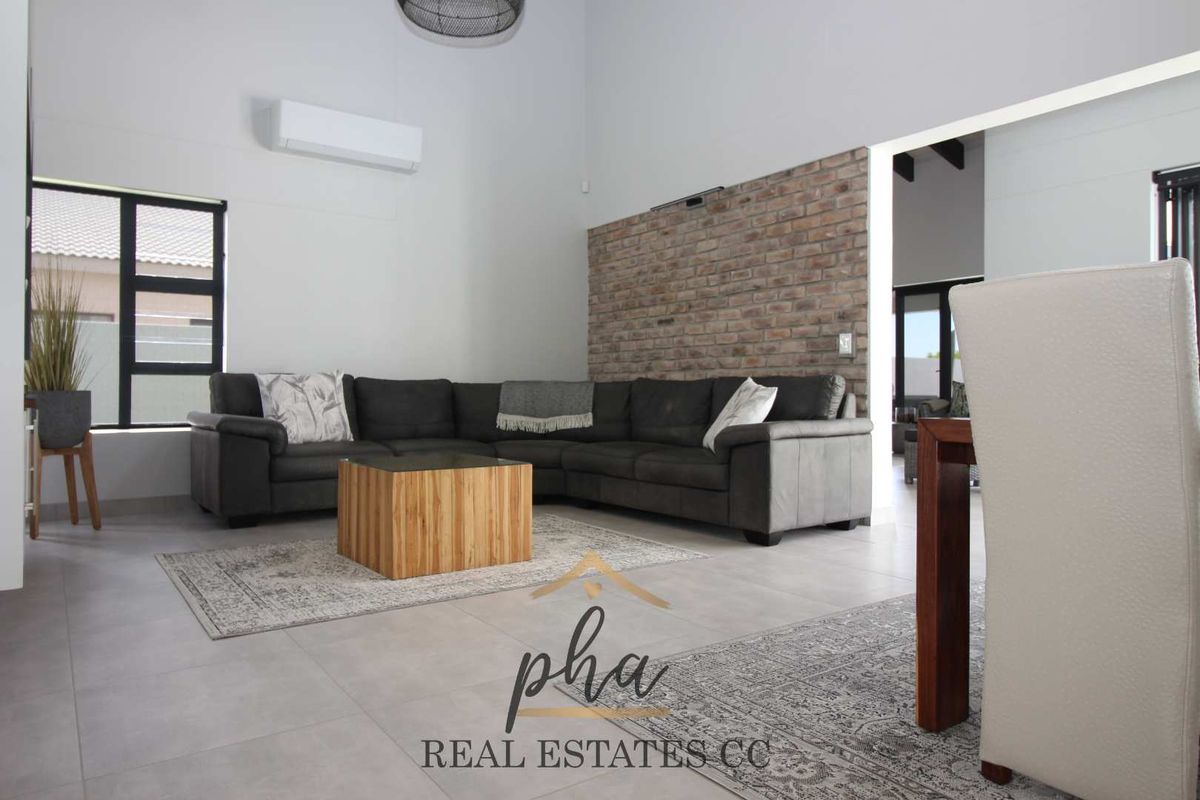 Spacious living area featuring high ceilings, a prominent exposed brick feature wall, tiled flooring, and a wall-mounted air conditioning unit.