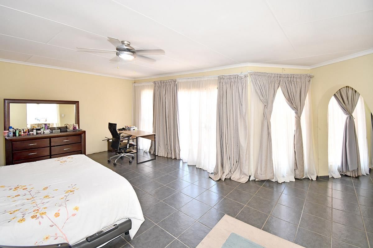 Spacious bedroom featuring large windows with floor-to-ceiling curtains, tiled flooring, and a ceiling fan.