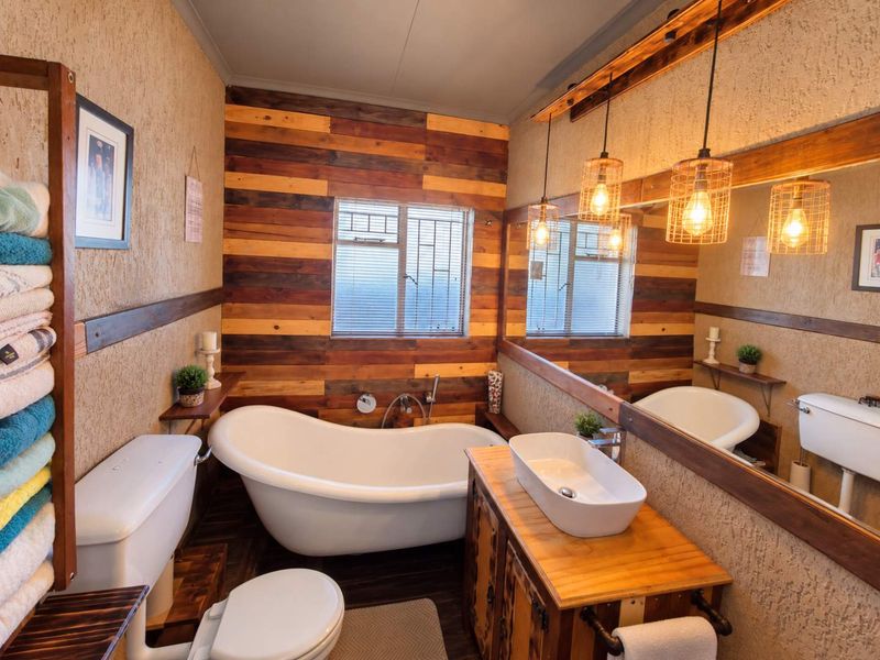 A rustic-style bathroom featuring a freestanding bathtub, vessel sink on a timber vanity, large mirror, and warm pendant lighting against textured and wood-clad walls.