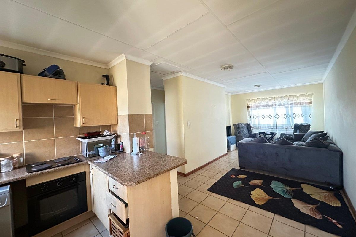 Open-plan living area featuring a functional kitchen with built-in cabinetry, oven, and hob, flowing into a tiled lounge space with natural light.