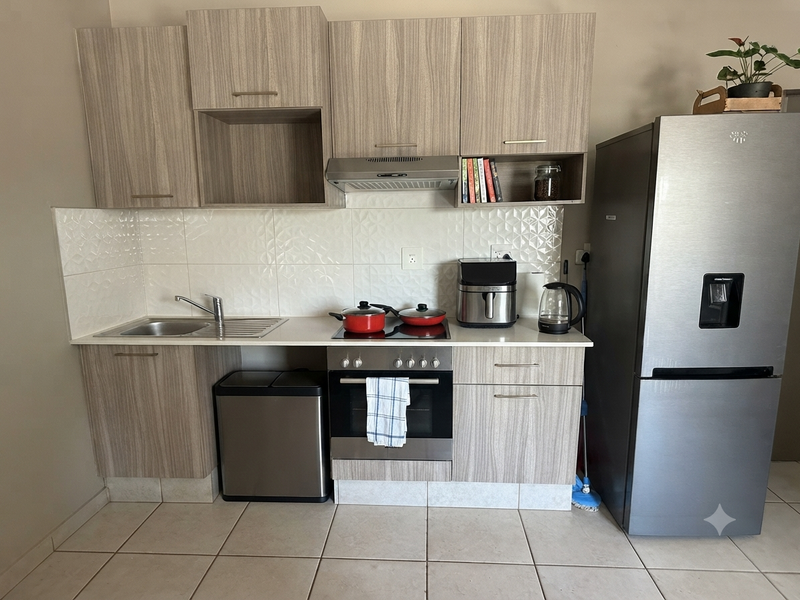 A compact, functional kitchen featuring modern wood-grain cabinetry, a built-in oven with hob, extractor fan, and tiled backsplash.