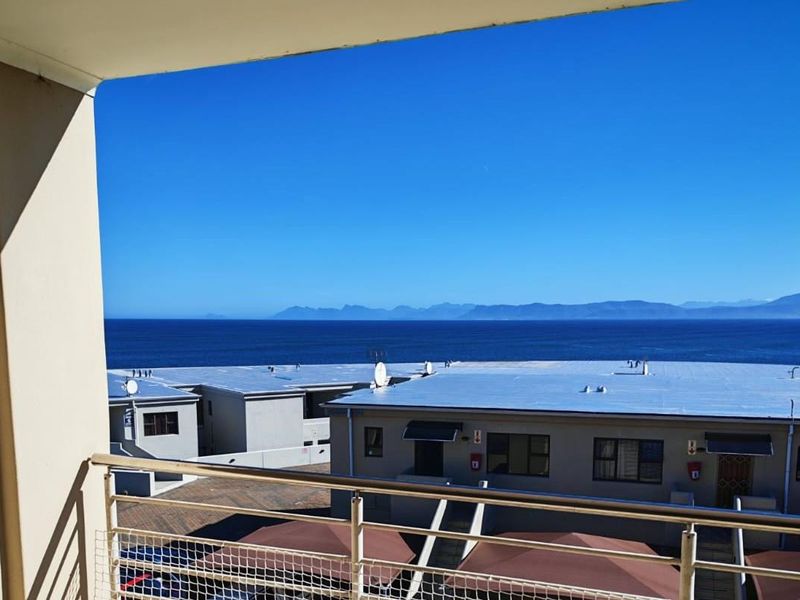 A clear elevated view of the ocean and distant mountains, captured from a balcony with a stainless steel balustrade.