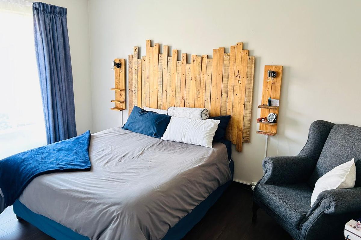 A bedroom featuring dark wood-look flooring, neutral walls, and a custom timber headboard with integrated shelving and lighting.