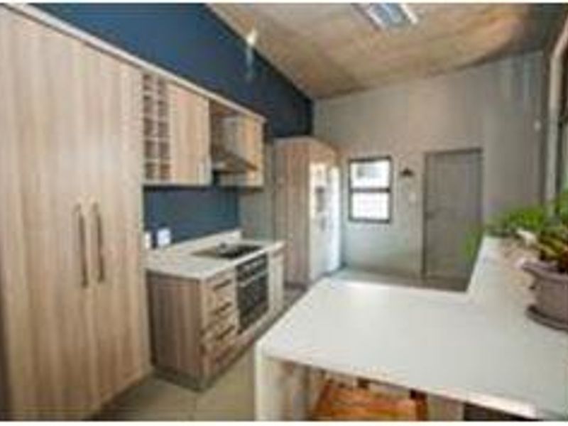 Modern kitchen featuring light wood cabinetry, stone countertops, integrated oven, and hob, with a breakfast bar and high ceilings.