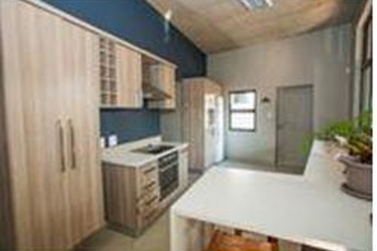 Modern kitchen featuring light wood cabinetry, stone countertops, integrated oven, and hob, with a breakfast bar and high ceilings.