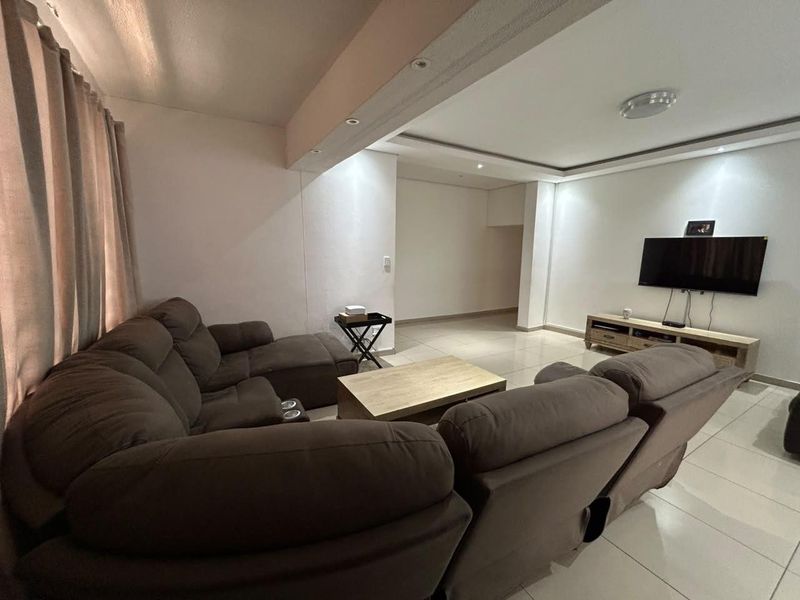 A spacious living room featuring tiled flooring, a bulkhead ceiling with recessed lighting, and a neutral color palette.