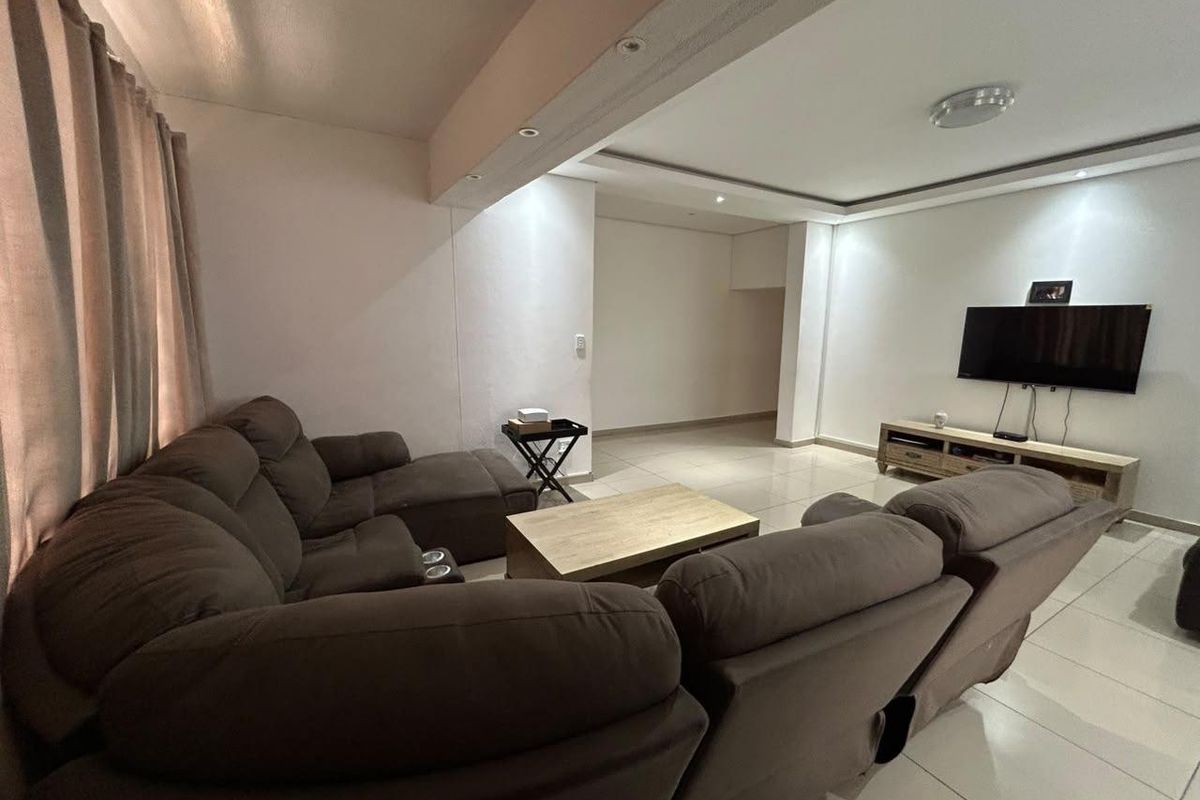 A spacious living room featuring tiled flooring, a bulkhead ceiling with recessed lighting, and a neutral color palette.
