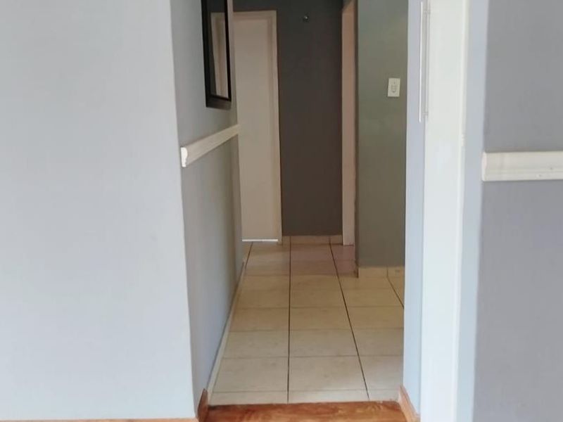 A clean, empty hallway featuring a transition between laminate and tiled flooring, finished with neutral grey walls and a chair rail.