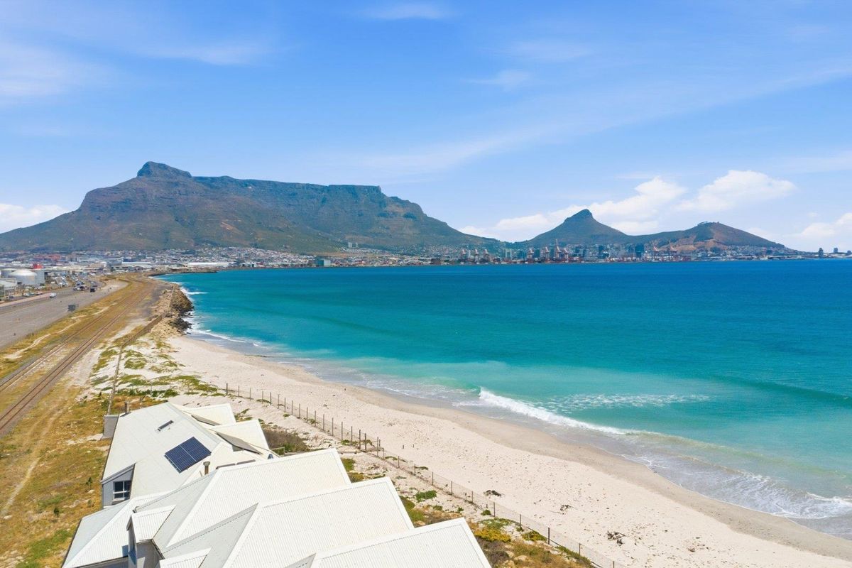 Aerial view of the coastal property featuring a metal roof with solar panels, overlooking the beach, ocean, and mountain range.