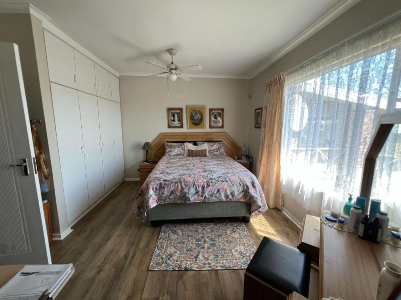 A well-lit bedroom featuring laminate flooring, built-in cupboards, and a ceiling fan, offering a functional and comfortable living space.
