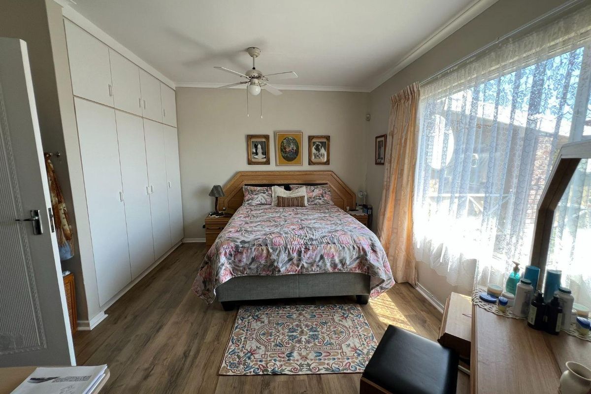 A well-lit bedroom featuring laminate flooring, built-in cupboards, and a ceiling fan, offering a functional and comfortable living space.