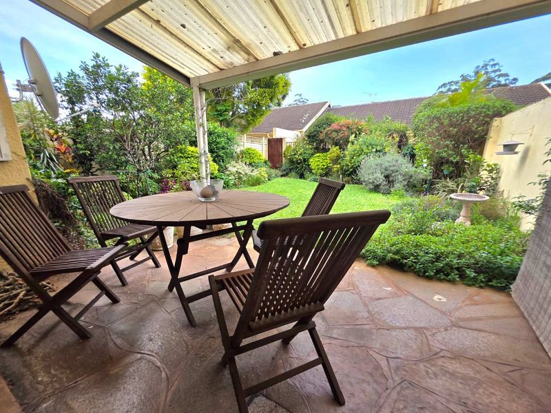 A covered patio area featuring flagstone paving, overlooking a well-maintained private garden with established landscaping and boundary walls.