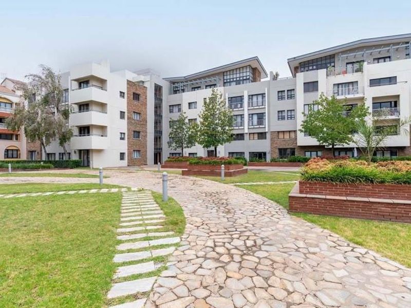 A well-maintained apartment complex exterior featuring a stone-paved garden path, landscaped brick planter boxes, and modern multi-story residential building facades.