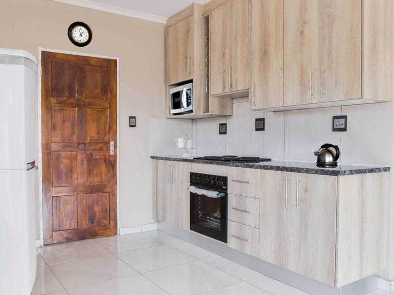 A functional kitchen featuring light wood-finish cabinetry, granite-look countertops, built-in oven and hob, and neutral tiled flooring.