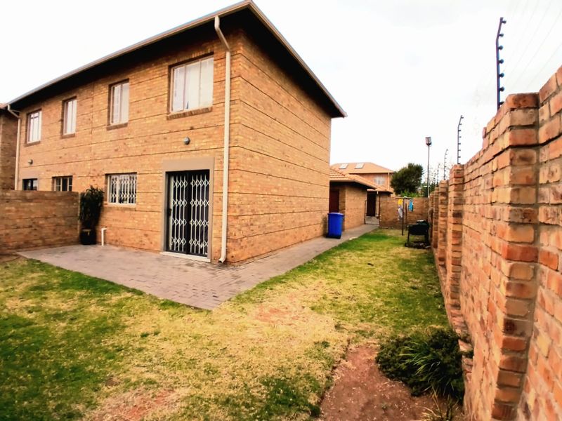 Rear view of a face brick townhouse featuring a paved patio area, private garden, and secure boundary wall with electric fencing.