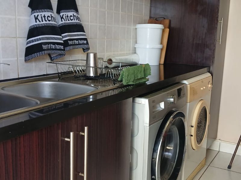 Functional laundry area featuring dark laminate cabinetry, a double bowl stainless steel sink, tiled backsplash, and dedicated plumbing connections for appliances.