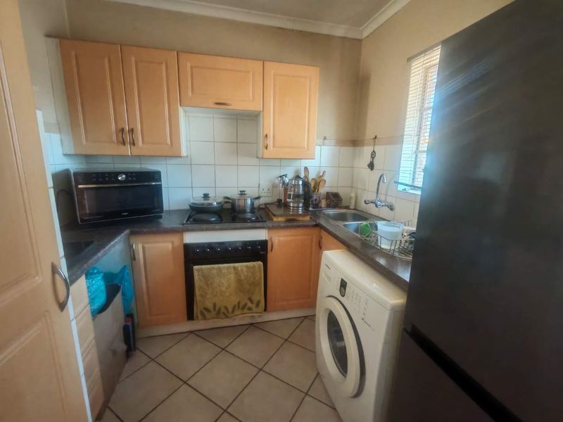 Compact kitchen featuring laminate cabinetry, tiled backsplash, built-in oven, electric hob, and a stainless steel sink with integrated laundry appliance space.