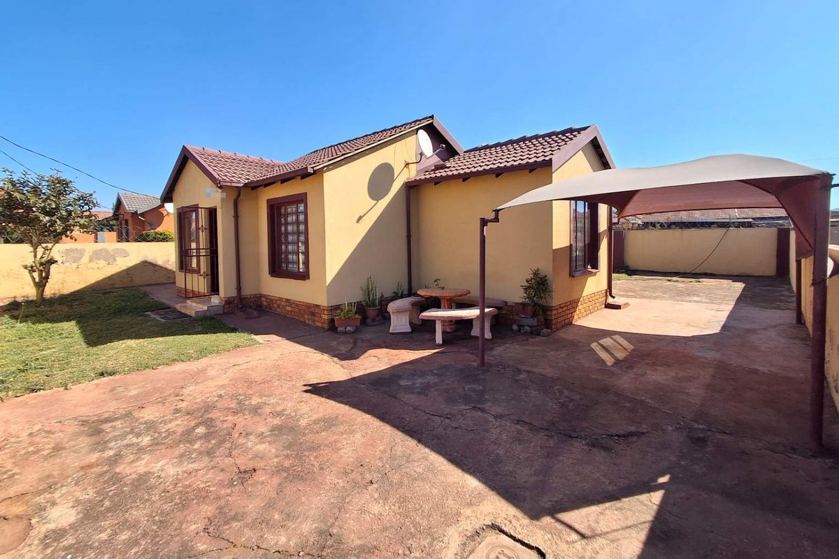 Rear view of the house featuring a concrete driveway, shade sail structure, and a private garden area with boundary walling.