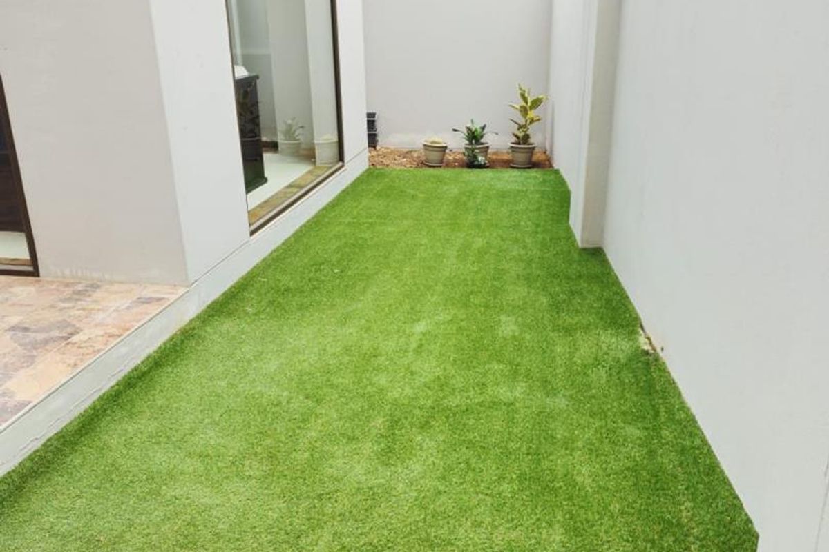 A neat, low-maintenance rear garden area featuring artificial turf, a high boundary wall for privacy, and direct access to the home via large glass doors.