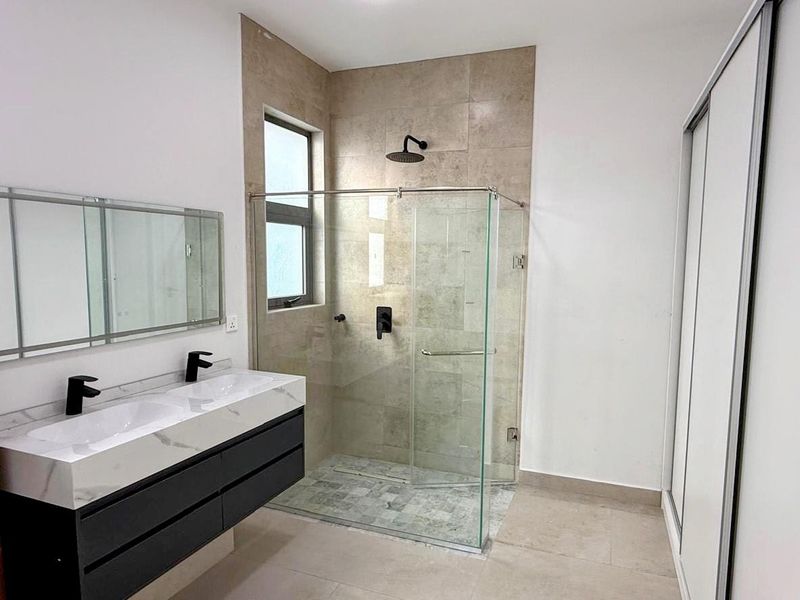 Modern bathroom featuring a double vanity with stone countertop, walk-in glass shower enclosure with rainfall showerhead, and built-in sliding door cabinetry.