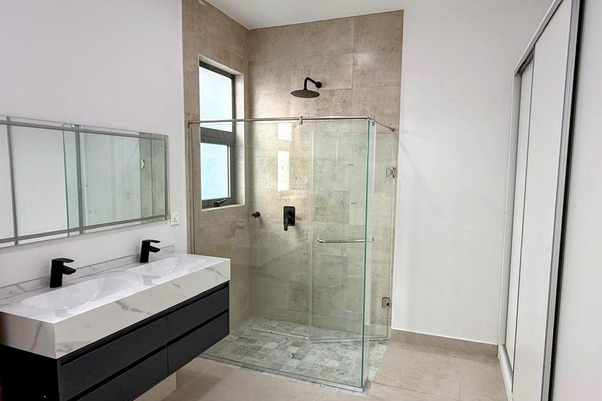Modern bathroom featuring a double vanity with stone countertop, walk-in glass shower enclosure with rainfall showerhead, and built-in sliding door cabinetry.