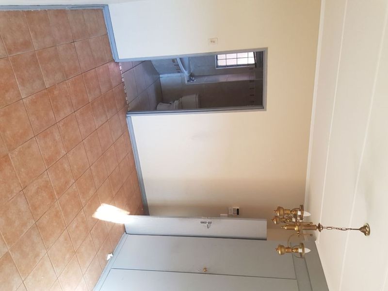 A vacant hallway featuring tiled flooring, a built-in cupboard, and access to an adjacent bathroom area.